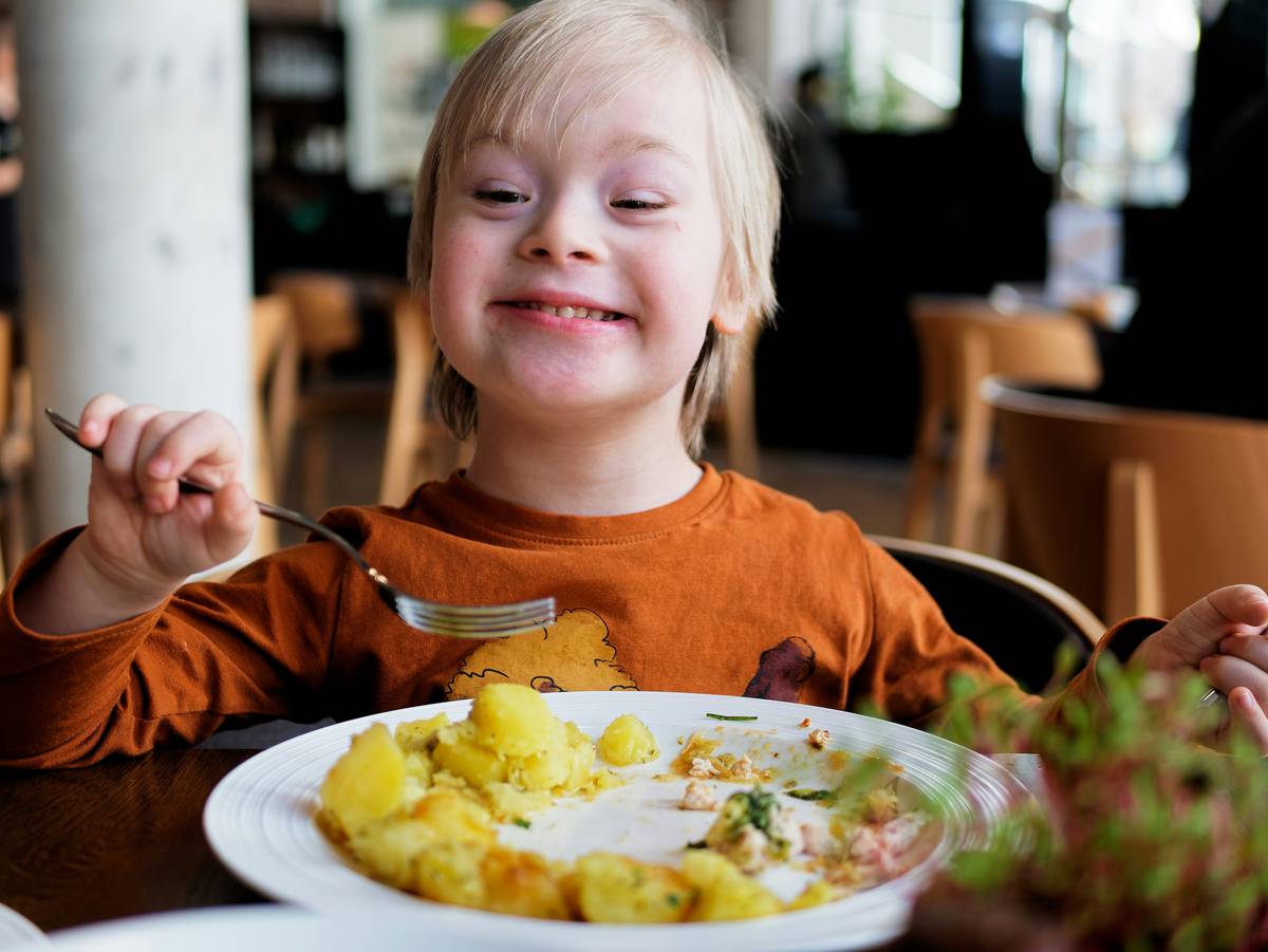 A young boy with Down's syndrome eats lunch in a restaurant.
